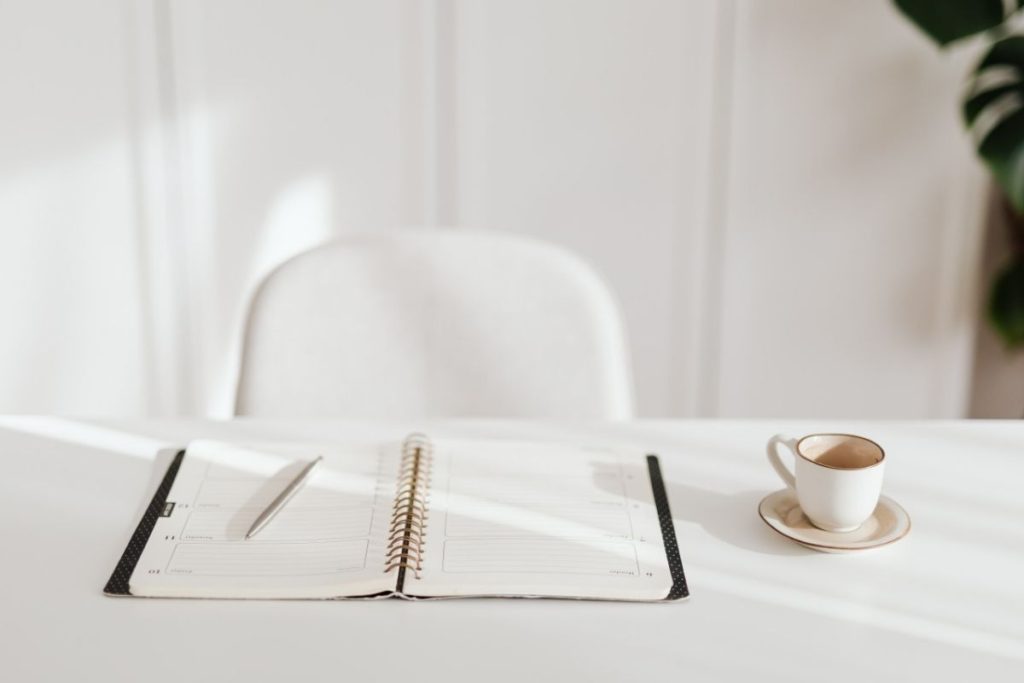 white desk and white chair with journal and pen and coffee