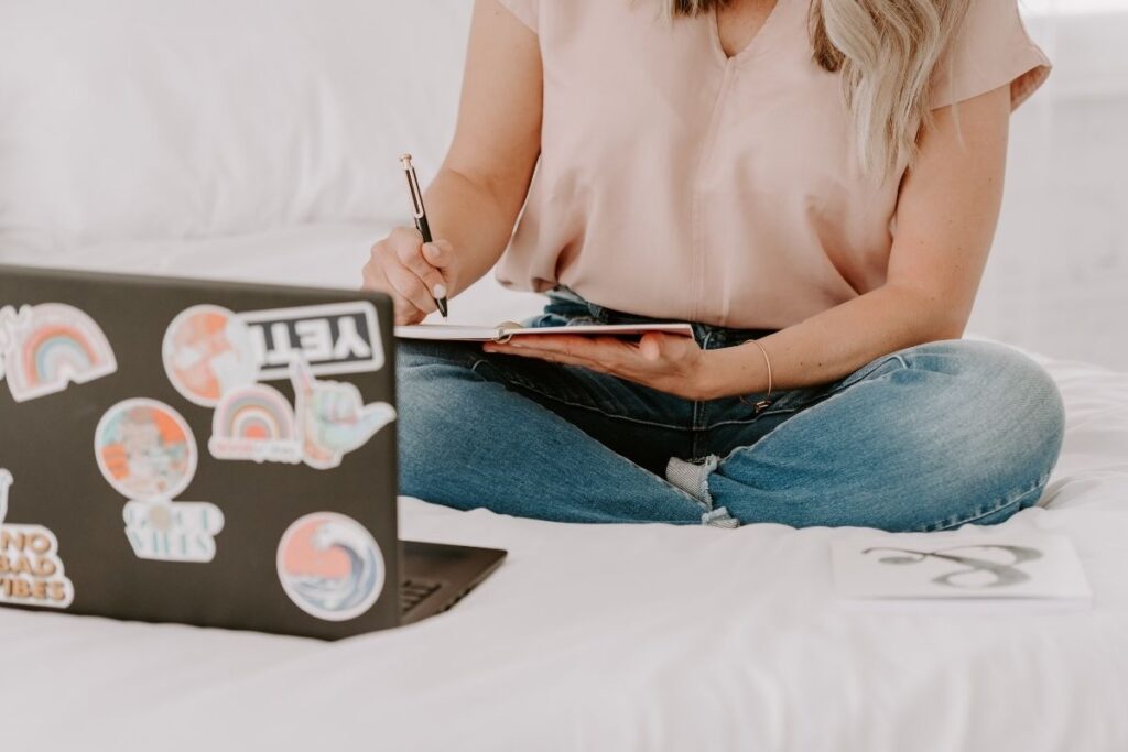 Girl in pink shirt journaling with laptop in front of her.