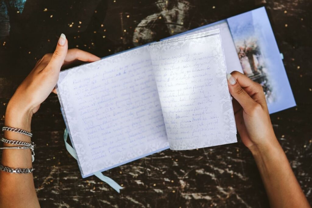 A woman flipping through a blue journal on a black backdrop.