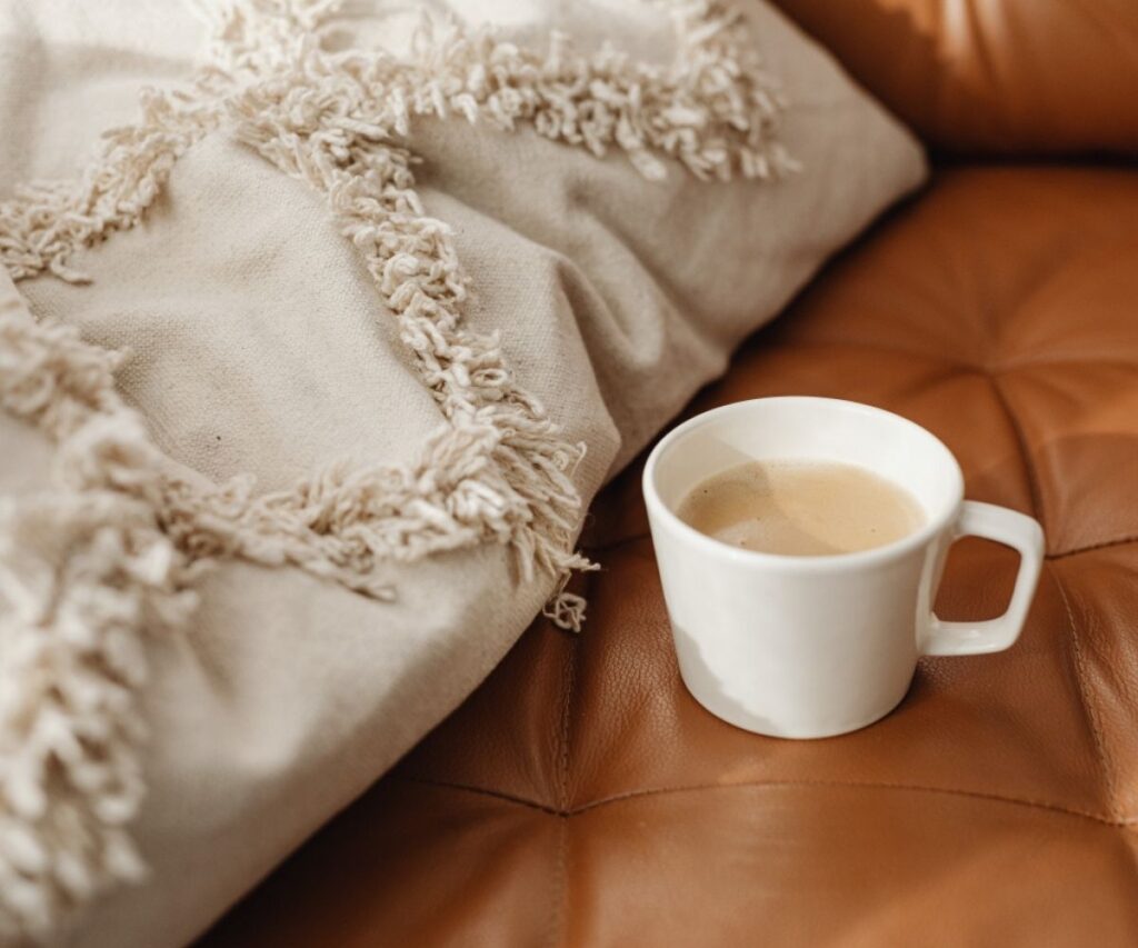 A white coffee mug sitting on an orange leather couch.