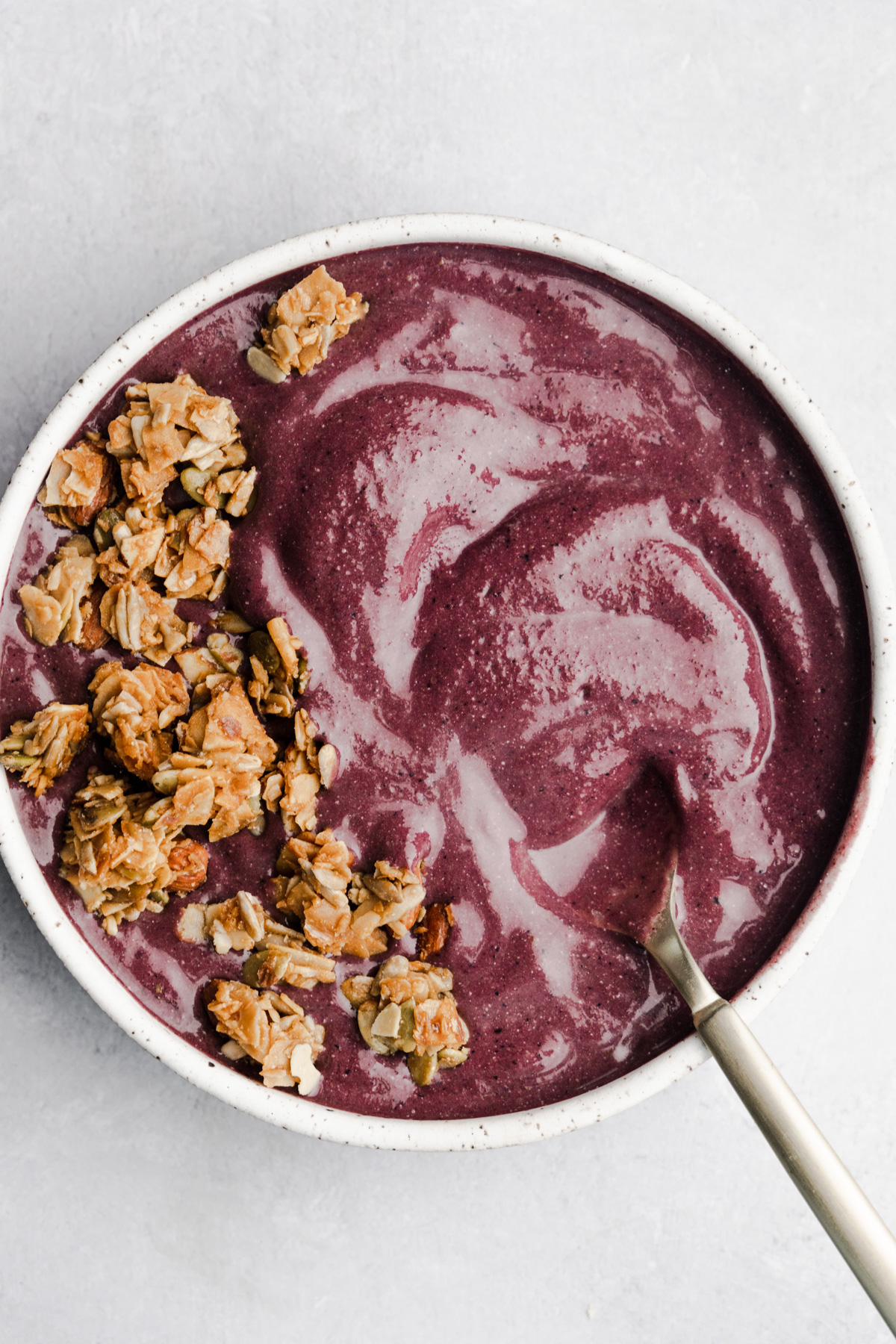 Acai berry bowl smoothie in a white bowl on a grey background.