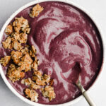 Acai berry bowl smoothie in a white bowl on a grey background.