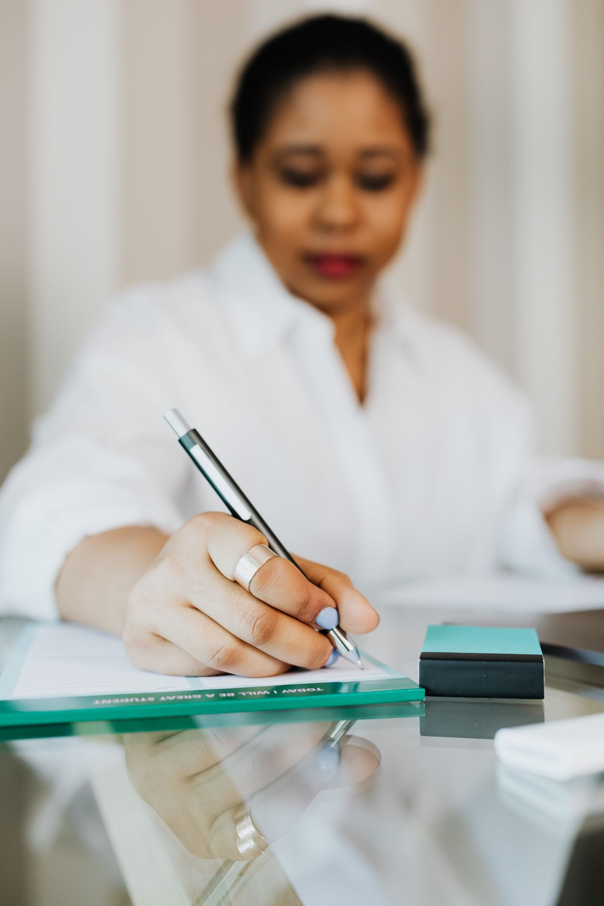 A woman writing on a notepad on a glass desk.