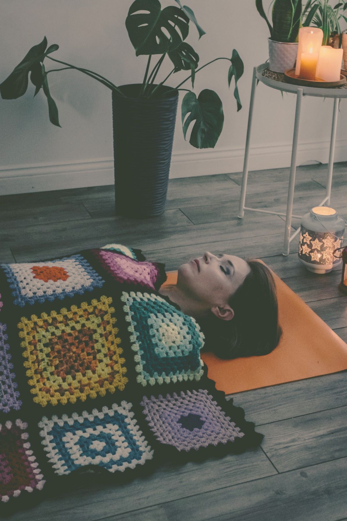 Woman resting in savasana on an orange yoga mat covered with a colorful blanket.
