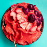 Strawberry Smoothie Bowl on a blue surface tipped with strawberries.