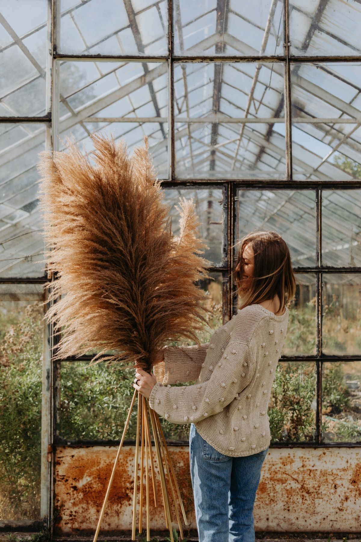 A woman outside in the fall holding grass.