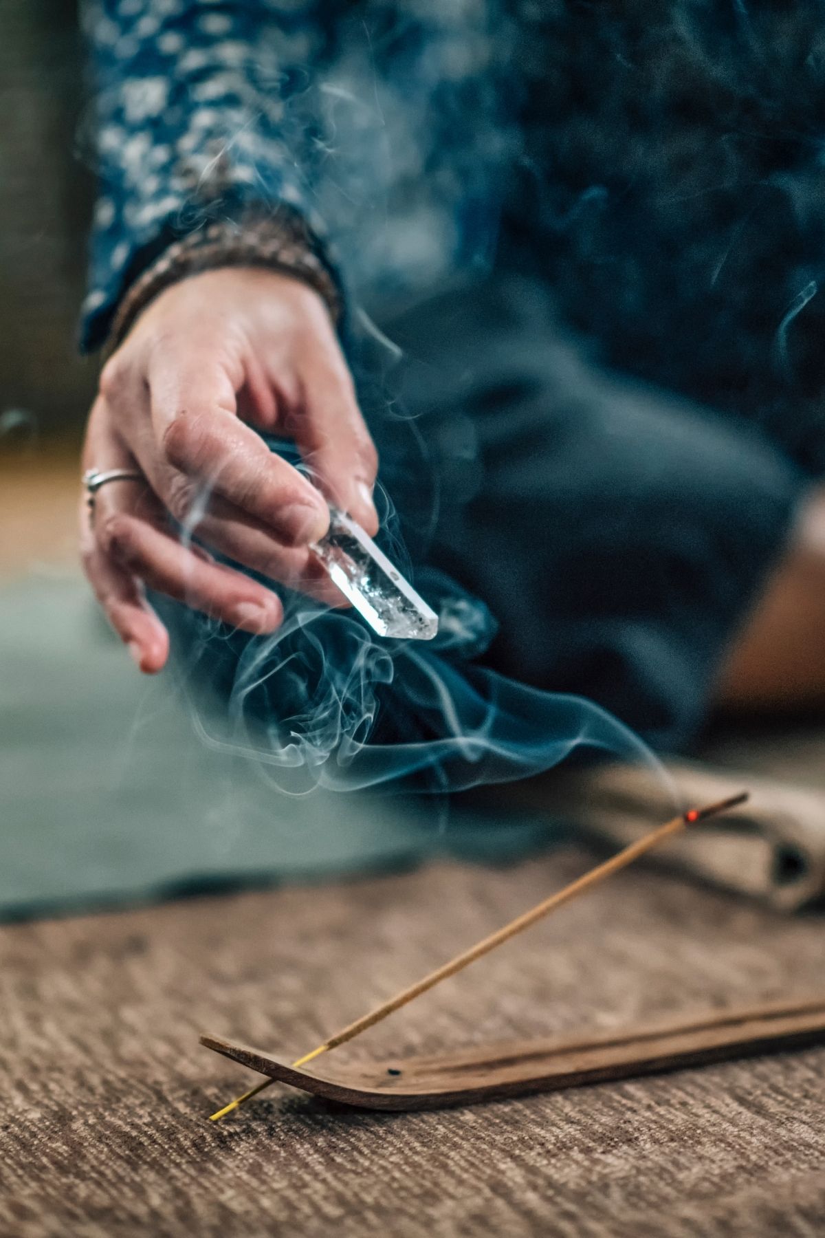 A hand cleansing a clear quartz crystal in inscense.