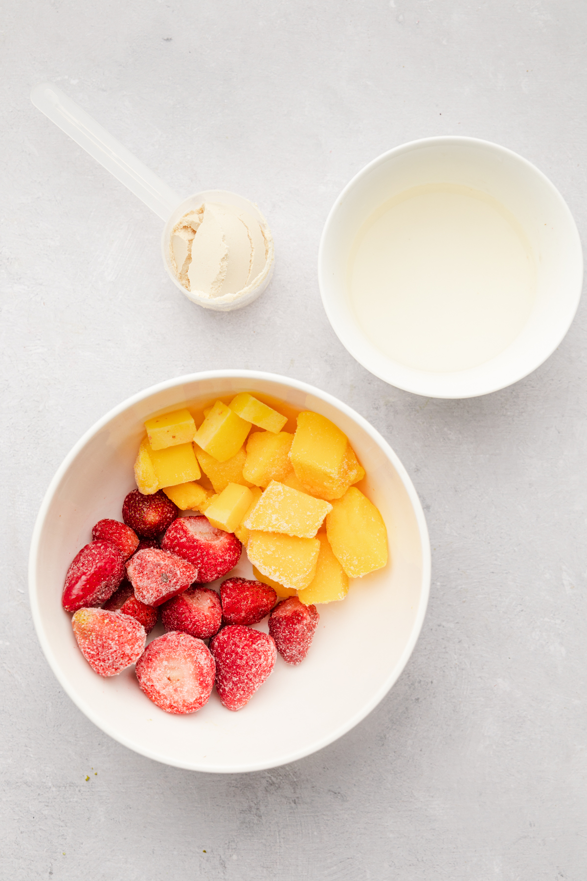 Ingredients for the strawberry mango smoothie bowl on a white surface.