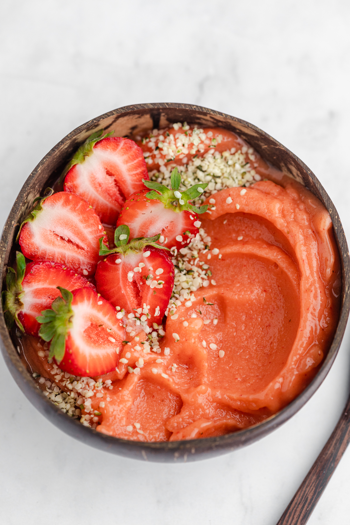 Strawberry mango smoothie bowl topped with hemp hearts and strawberries in a coconut bowl.