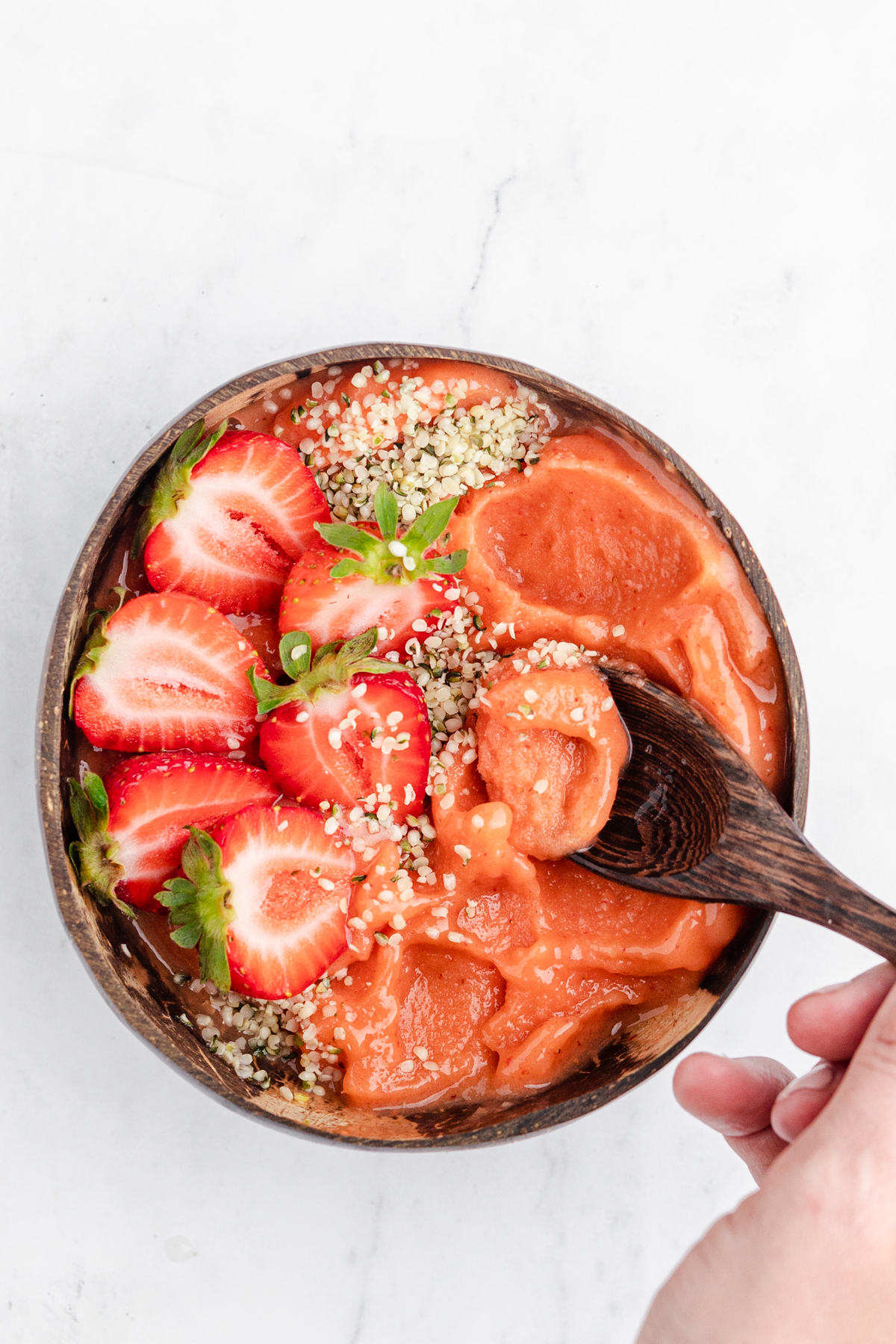 Strawberry mango smoothie bowl topped with hemp hearts and strawberries in a coconut bowl being scooped out.