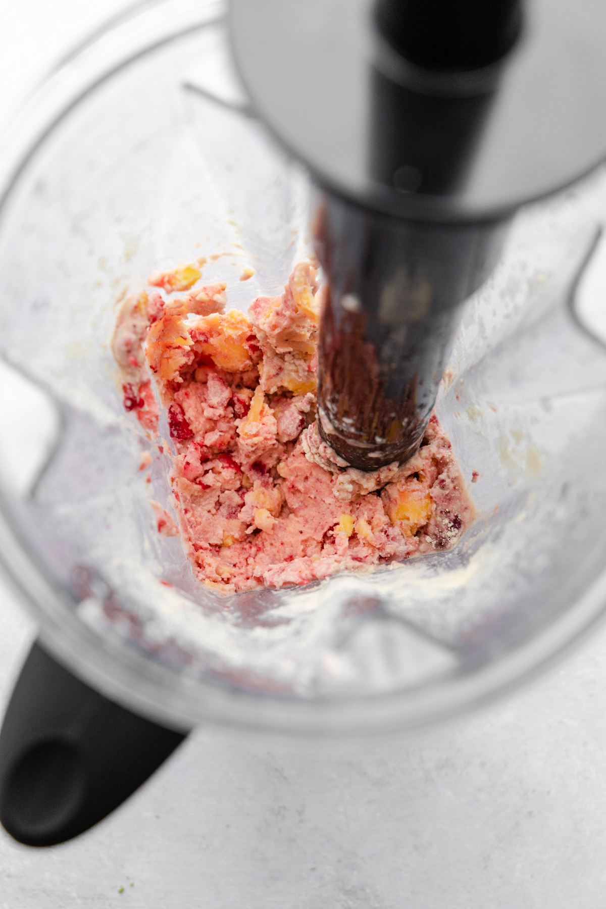 Strawberry mango smoothie bowl in blender halfway thru blending.