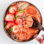 Strawberry mango smoothie bowl topped with hemp hearts and strawberries in a coconut bowl.