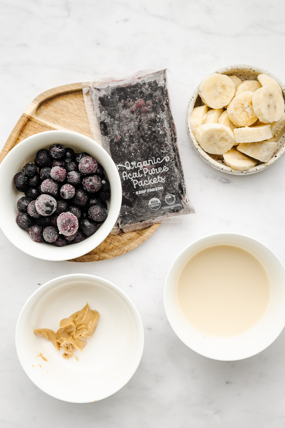 Ingredients on a white table for peanut butter acai bowl.