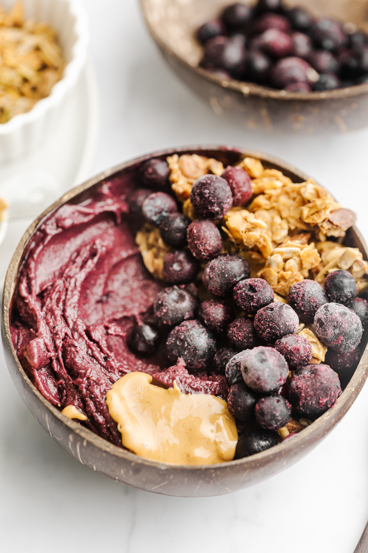 A table of acai bowls topped with frozen blueberries, granola and peanut butter drizzle.