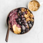 Peanut butter acai bowl in a coconut bowl with a side of peanut butter.