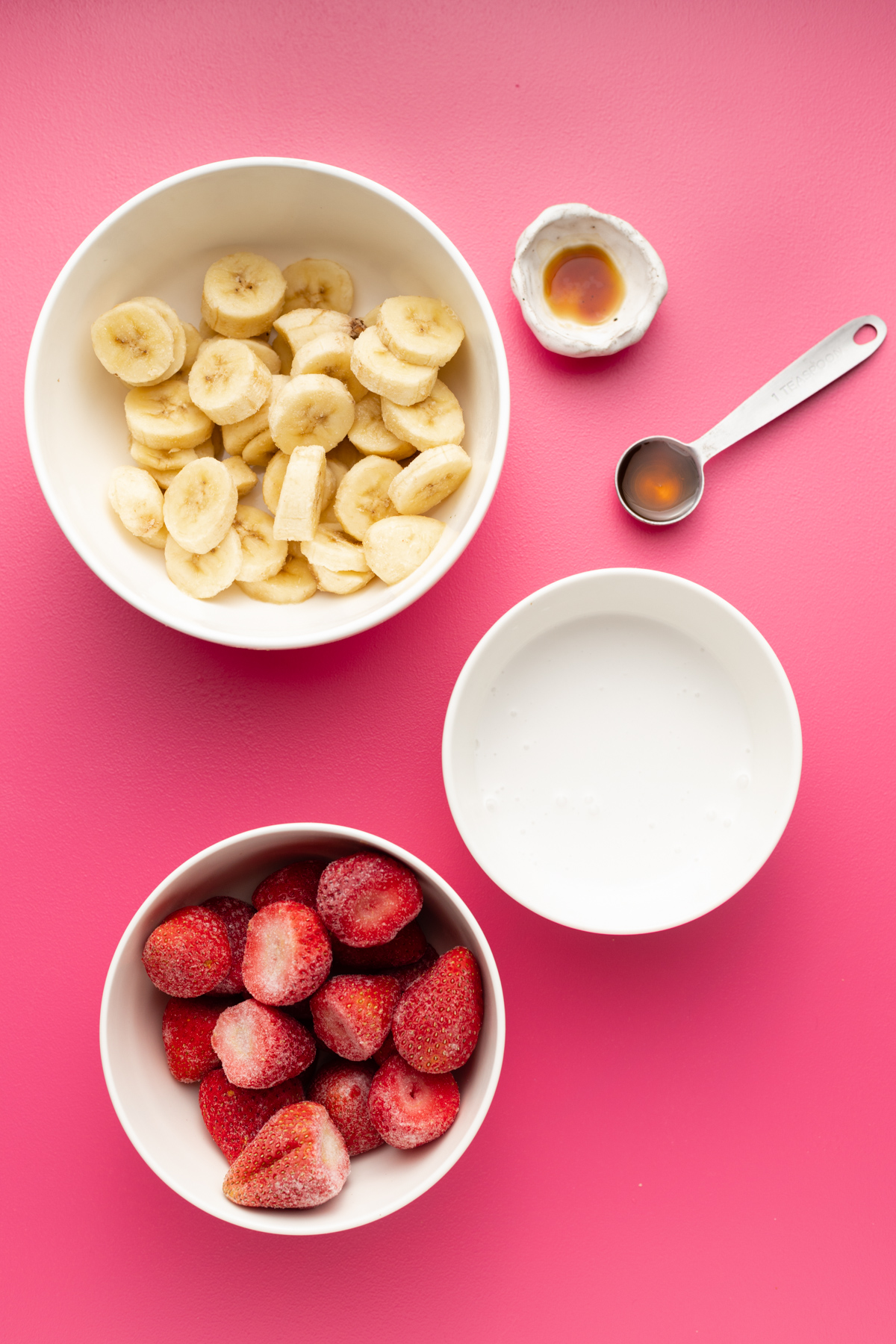 Ingredients for strawberry banana no yogurt smoothie bowl on a pink surface.
