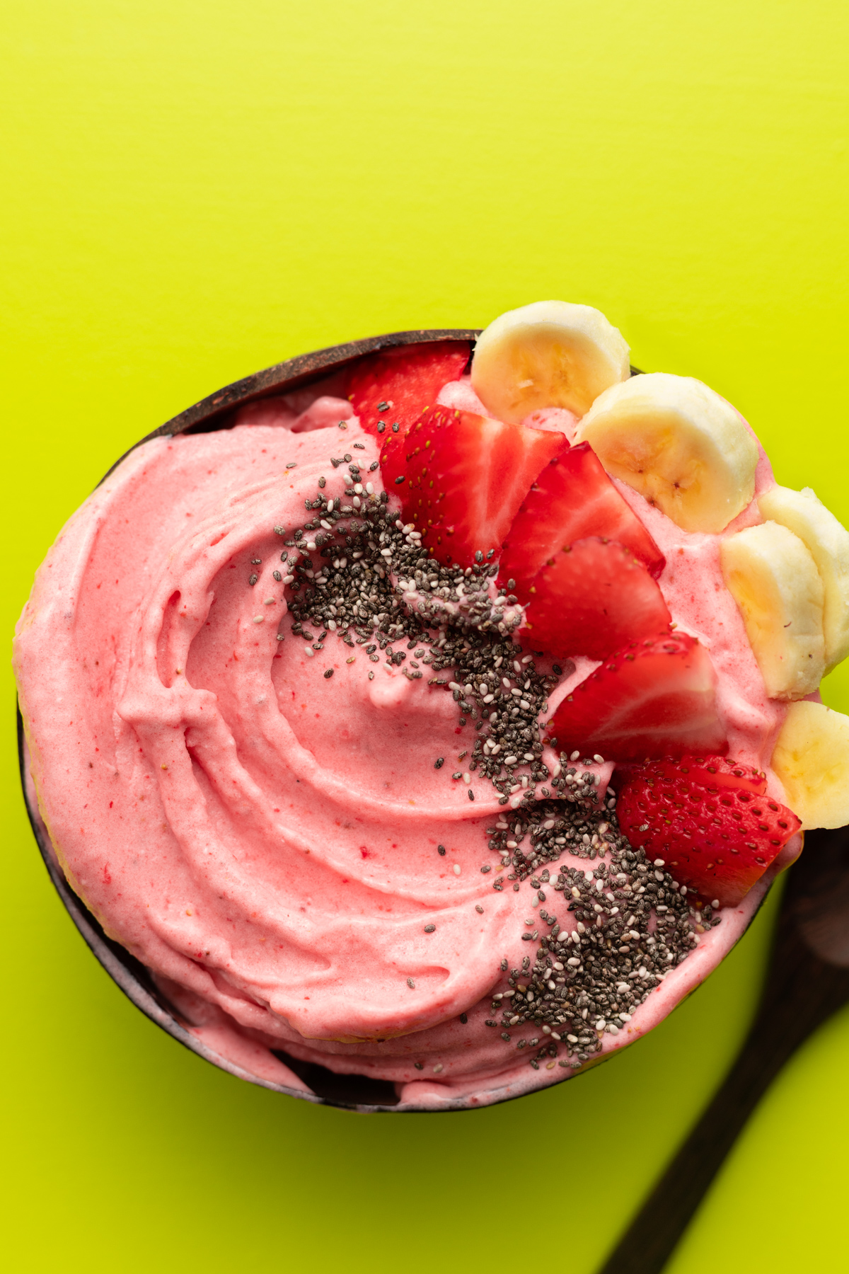 Strawberry banana smoothie bowl in coconut bowl on a green surface.