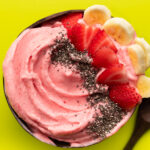 Strawberry banana smoothie bowl in coconut bowl on a green surface.