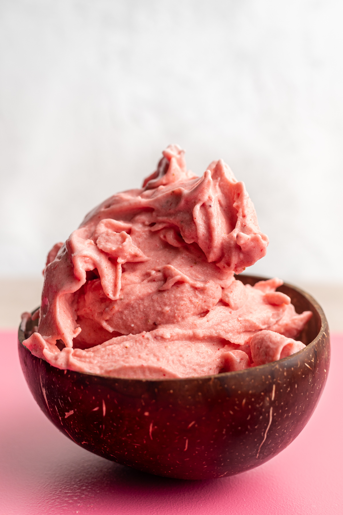 Strawberry banana smoothie bowl in coconut bowl piled high like thick ice cream.