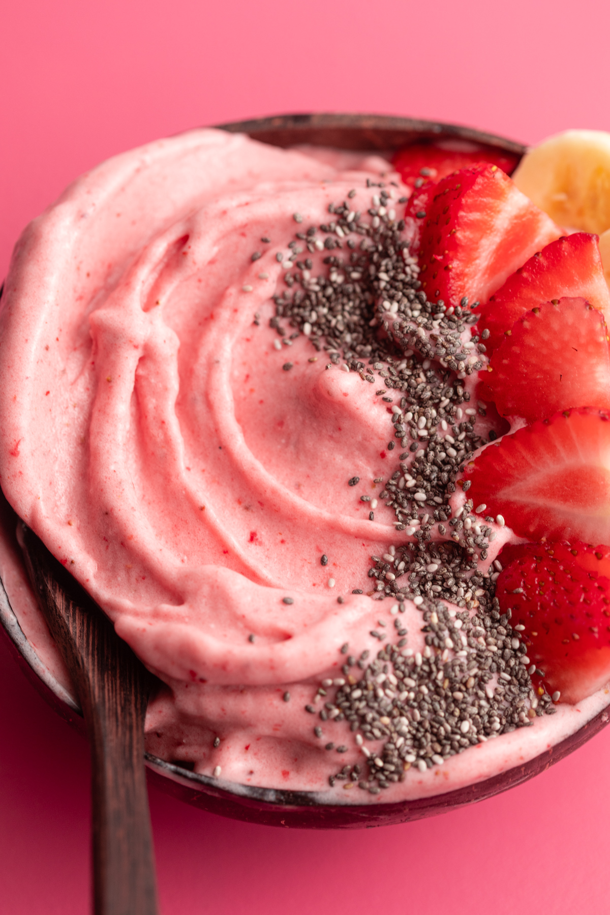 Strawberry banana smoothie bowl in coconut bowl on a pink surface.