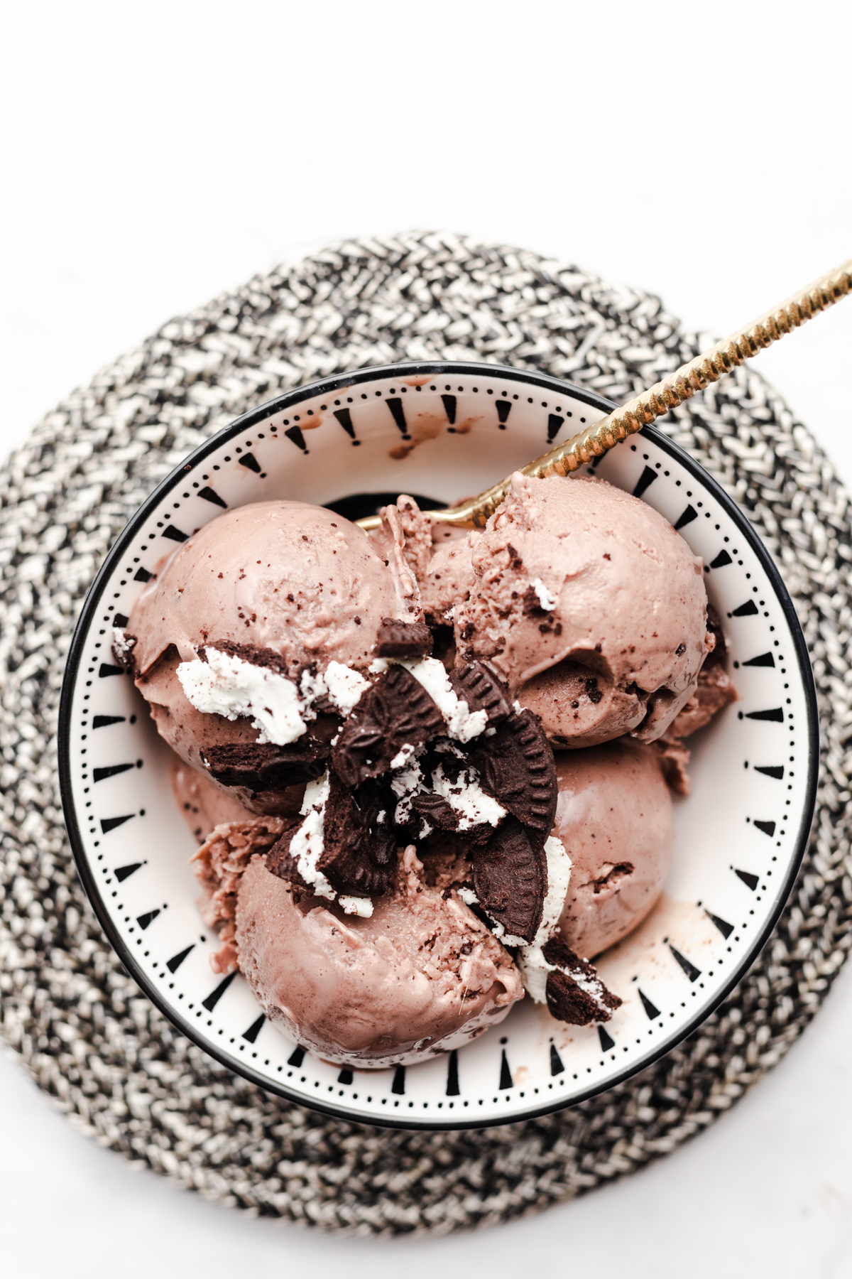 Overhead view of scoops of chocolate mint healthy creami ninja ice cream in a black and white bowl on a black and white trivet. Topped with oreo cookies.