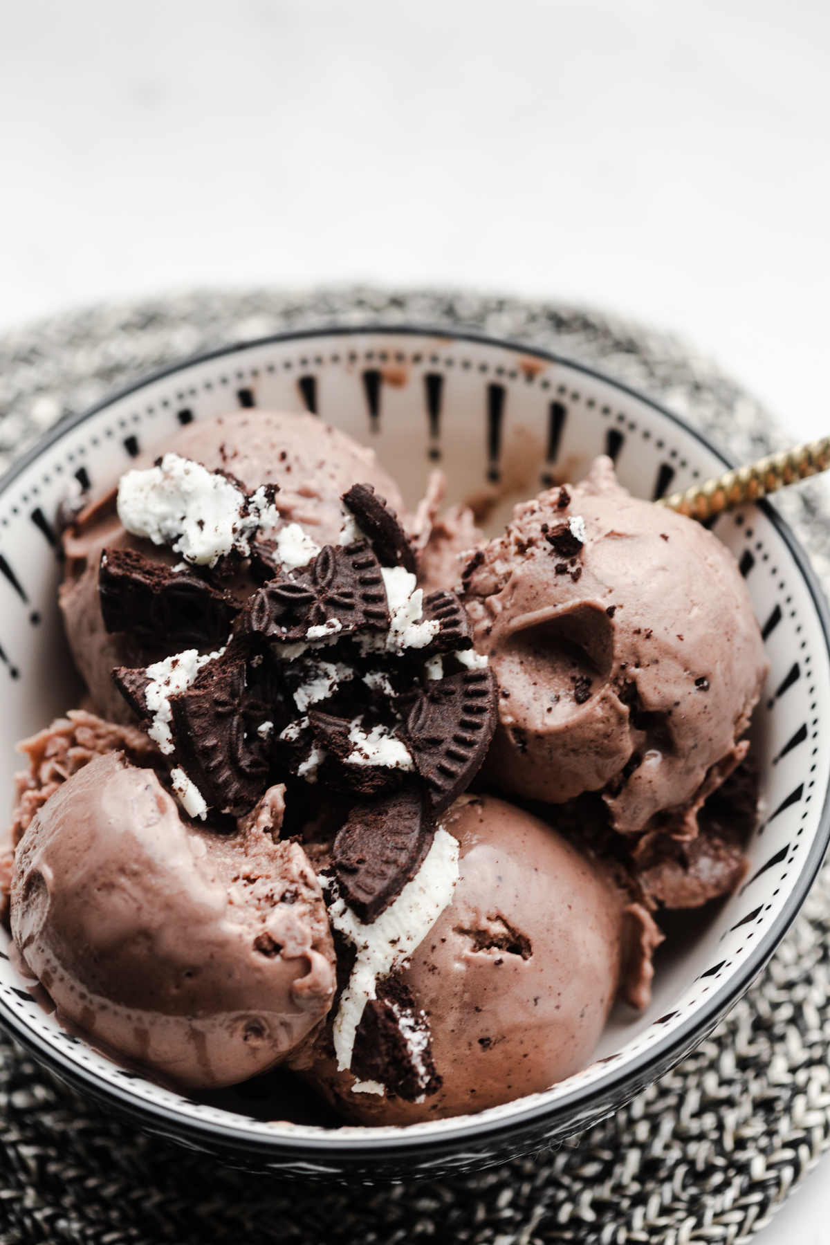 Side view of scoops of chocolate mint healthy creami ninja ice cream in a black and white bowl on a black and white trivet. Topped with oreo cookies.